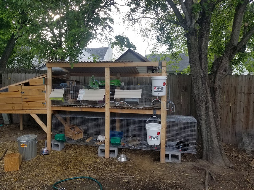 Initial rabbit cage set up with hutch on upper run, leaking water system and cinder block support on bottom cage. Poor design