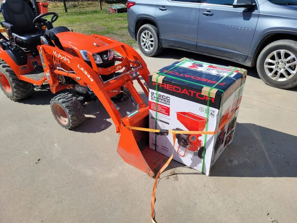 OrangeSubcompact Tractor with Wood chipper strapped to bucket